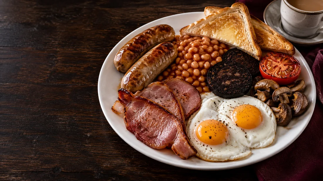 Een compleet English breakfast met worstjes, back bacon, eieren, bonen, tomaat, champignons en toast.